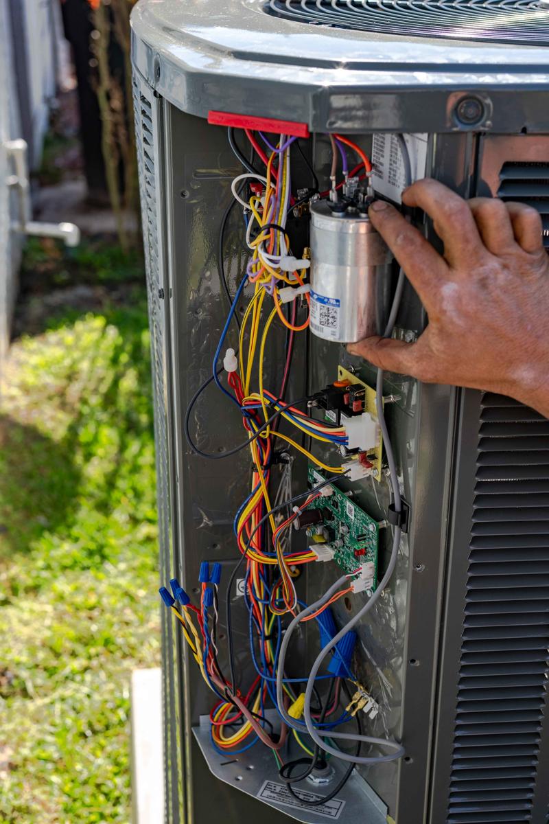 A Custom Air Conditioning Air Quality technician inspects the internal wiring and components of an outdoor air conditioning unit ensuring proper AC service and repair 2